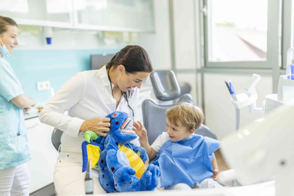 Zahnärztin Dr. Stegherr mit einem Plüschtier und einem lachenden Kind im Behandlungszimmer.