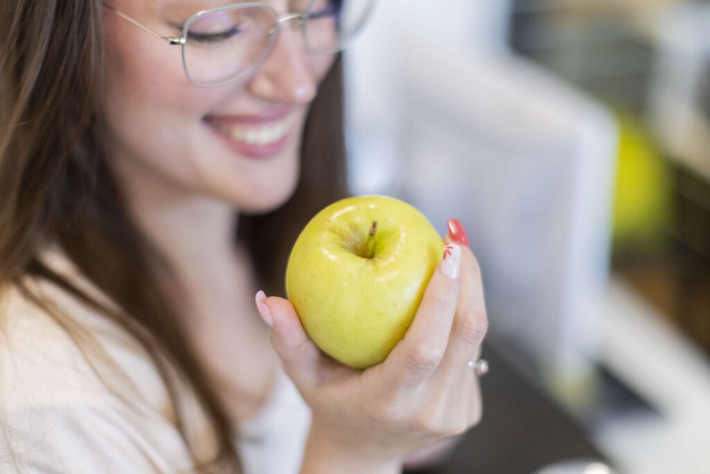 Eine junge Dame mit gesunden Zähnen hält einen knackigen Apfel in der Hand.