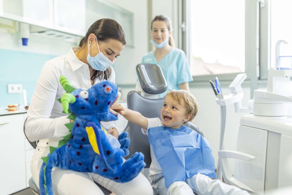 Frau Dr. Stegherr mit einem Plüschtier auf dem Schoß, erklärt einem Kind etwas über Zahngesundheit.