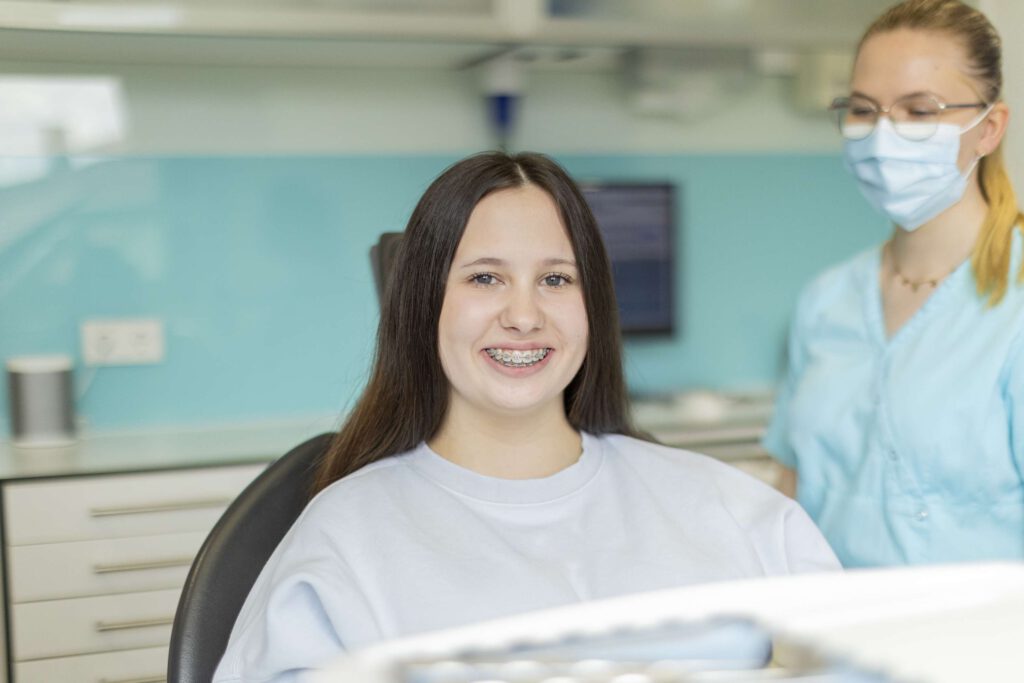 Eine Patientin im Behandlungsstuhl lächelt freundlich mit Zahnspange.