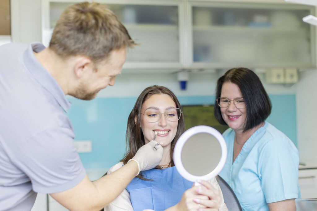 Die Patientin lächelt in den Spiegel. Die Farbe wird genau vom Zahntechniker und einer Assistentin abgestimmt.